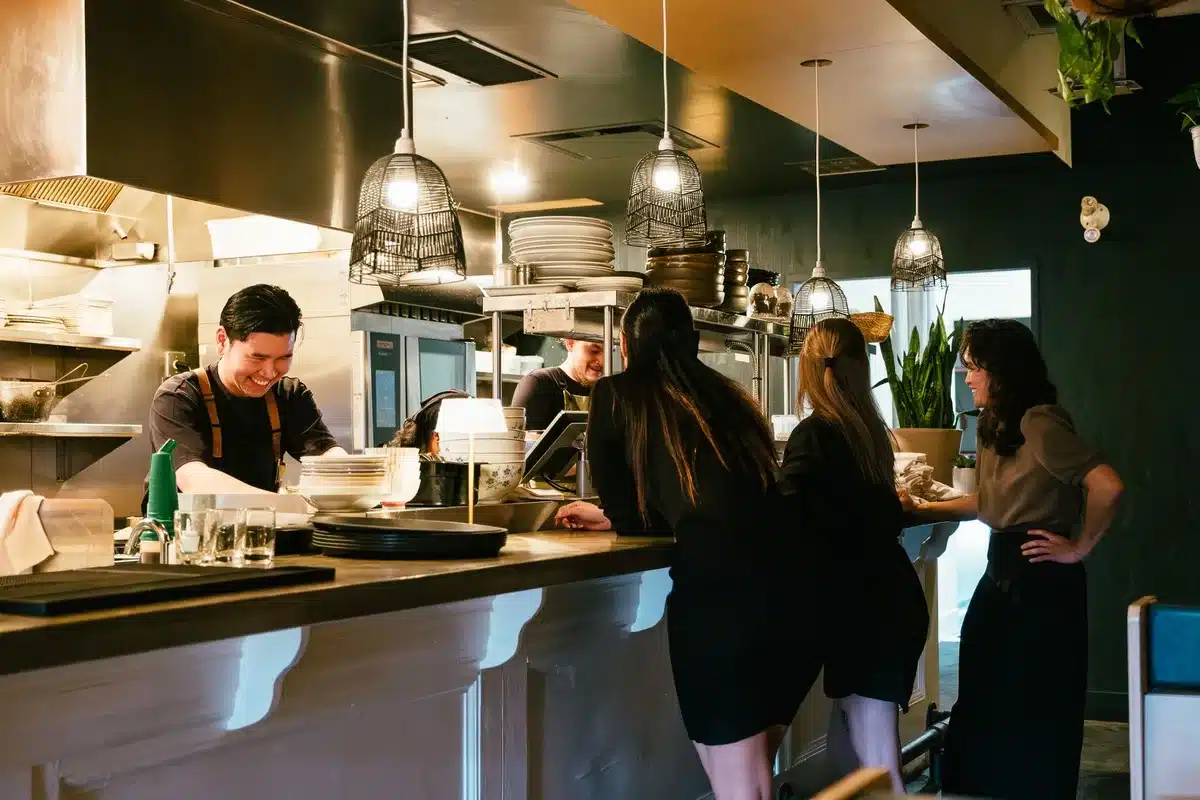 Chef interacting with diners at an open kitchen counter during a tasting menu service.