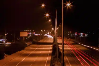 Car driving on an open road at dusk with a hotel silhouette visible in the distance ahead.