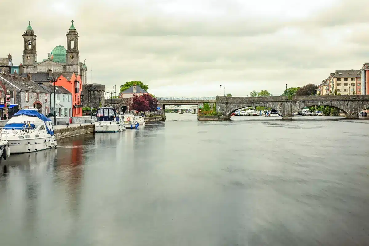 Báid chruisí ar an Shannon, ag soilsiú mall ar an abhainn le baile beag ar an bhruach