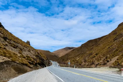 Dramatic New Zealand landscape with mountain peaks, rolling hills and winding road through native forest