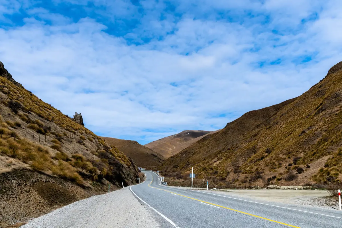 Dramatic New Zealand landscape with mountain peaks, rolling hills and winding road through native forest