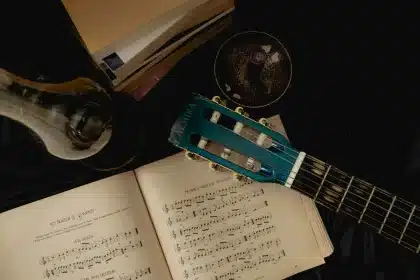 A guitar, handwritten lyrics, and tea cup on a wooden table in soft light