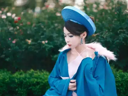 Woman in elegant dress and hat walking through a sunlit racecourse paddock