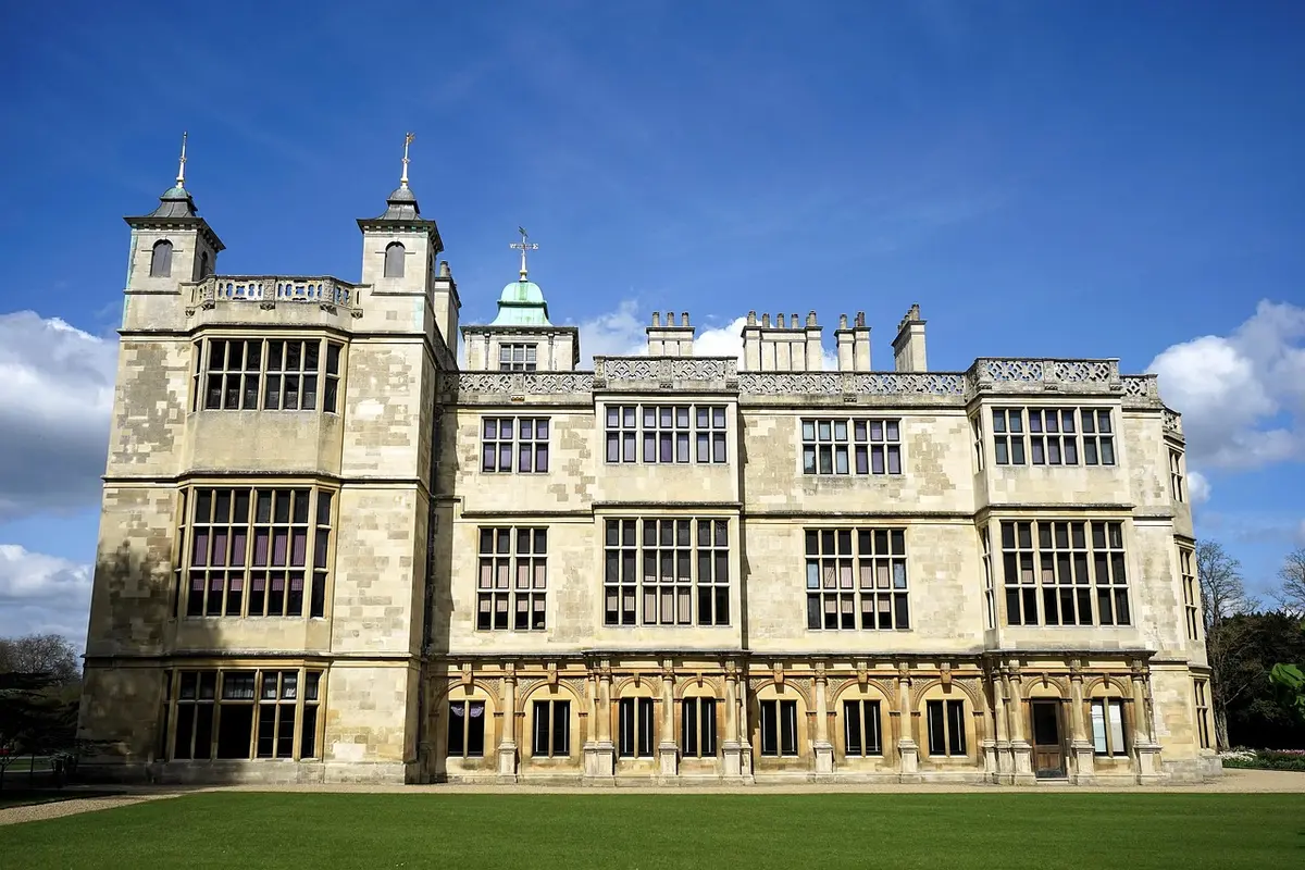 Historic manor house with manicured lawns overlooking a lake in bright daylight