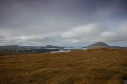 Daytime view of a fjord inlet with rocky peaks and distant hikers in Connemara