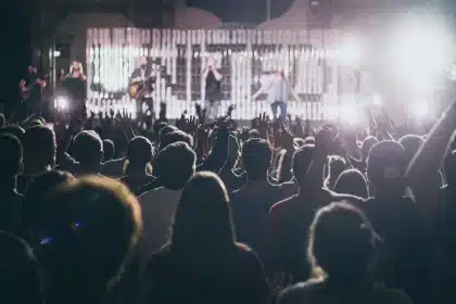 Crowd in sequins and neon at a rainy outdoor festival, silhouetted hands raised
