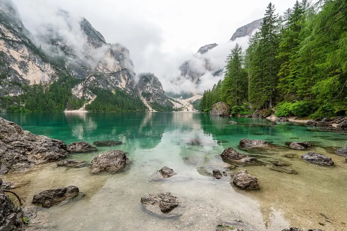 Kayaker paddling over crystal-clear water with steep mountain cliffs reflected below
