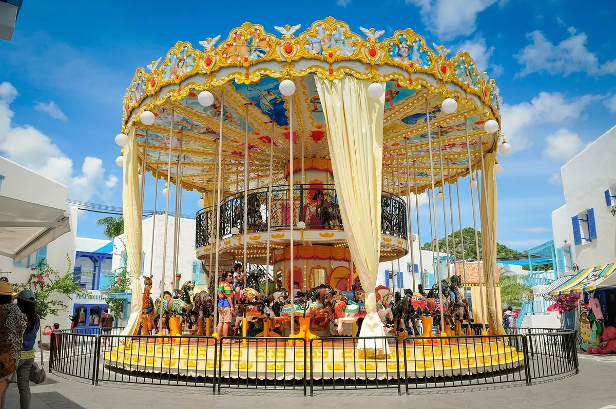 A vintage carousel at a fairground with families nearby in daylight