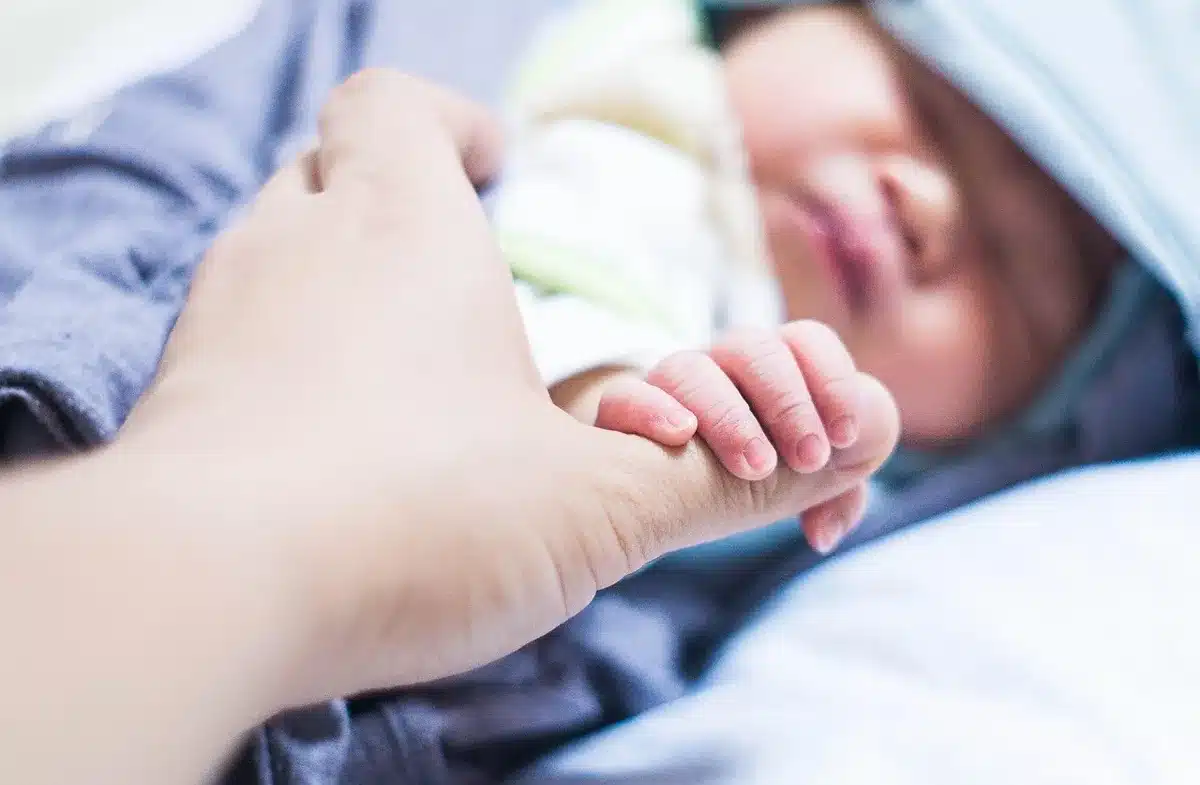 Parents' hands and a folded baby blanket in a sunny living room